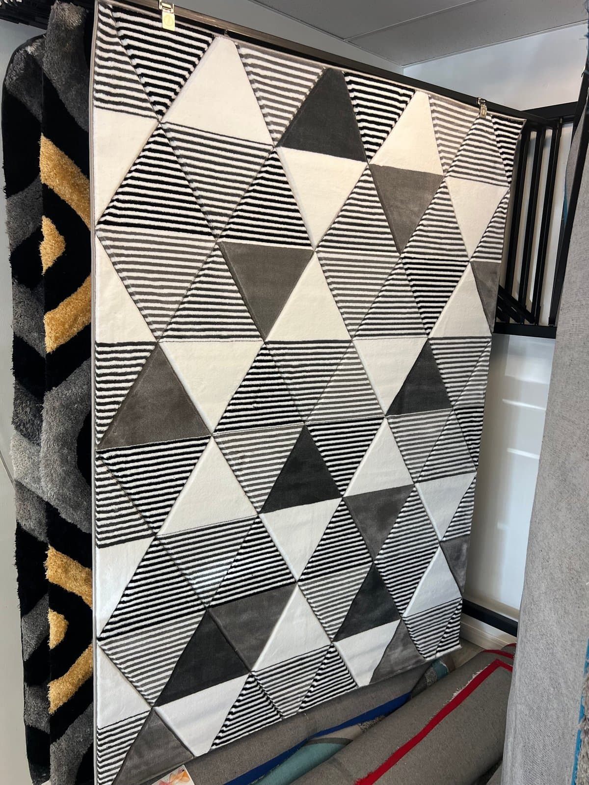Geometric black and white striped triangular pattern rug displayed in a showroom with other textiles visible on the sides
